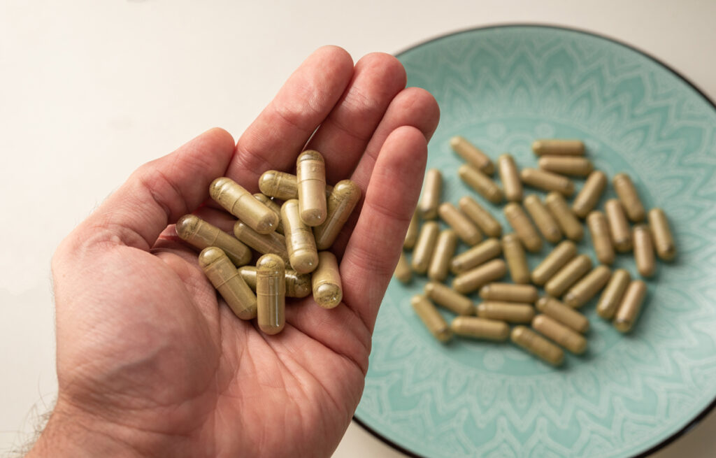 A hand holding kratom capsules focuses on kratom benefits and raises curiosity about what does kratom feel like